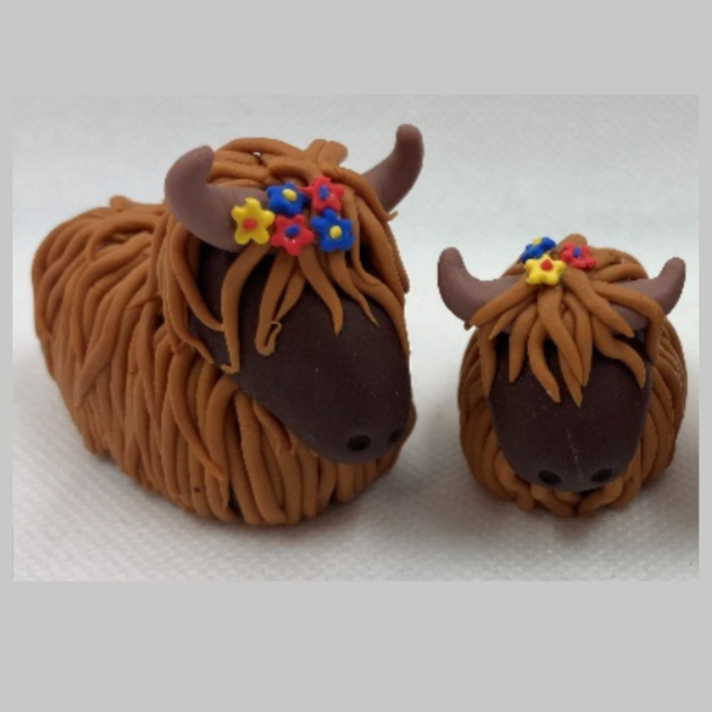2 Highland cows made from polymer clay with small flowers in their hair