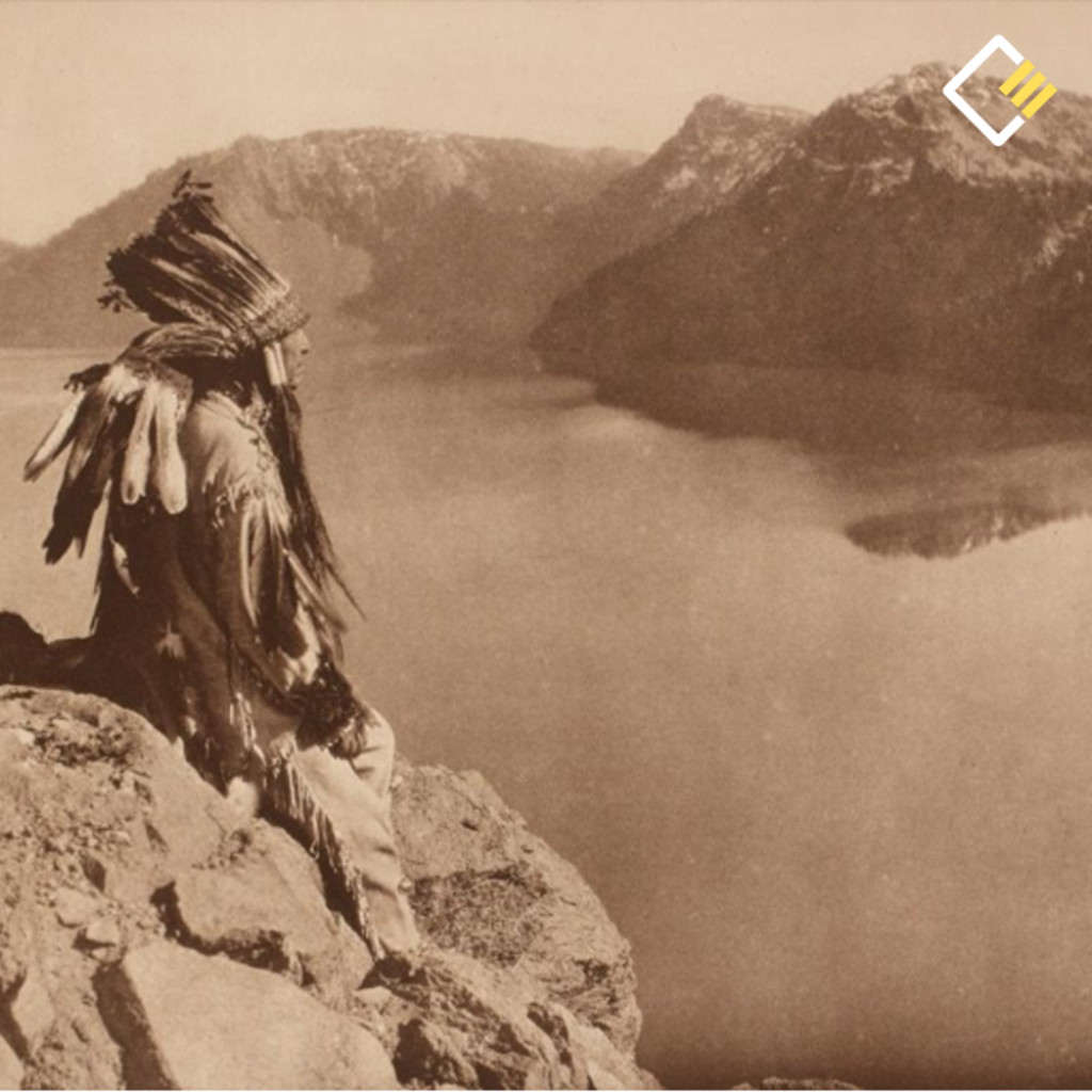 A person in traditional attire sits on a rocky cliff, overlooking a serene lake with mountain peaks in the background. The scene feels contemplative.
