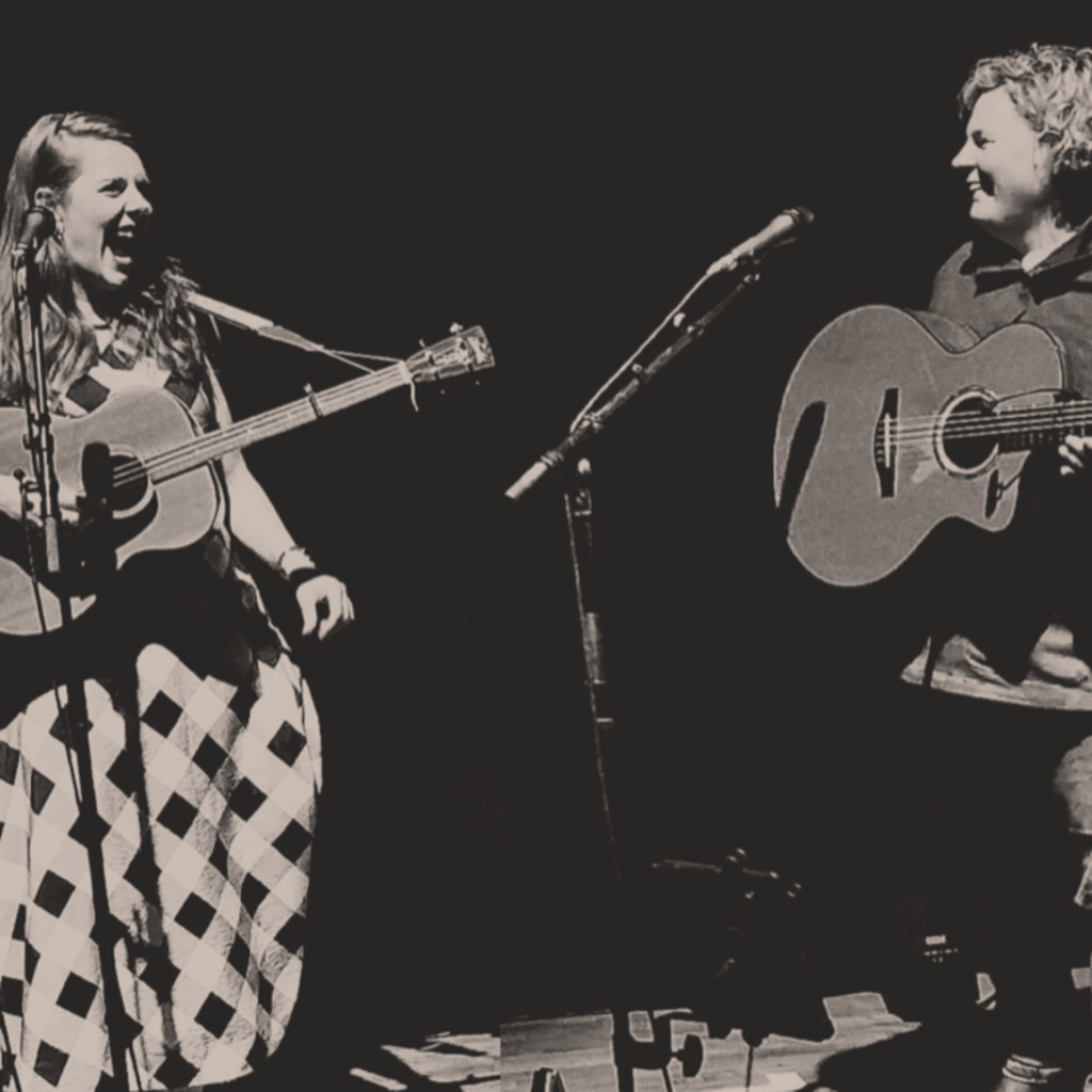 The image features Hannah Rarity and Anna Massie in sepia tones standing and performing while looking at each other with joyful expressions