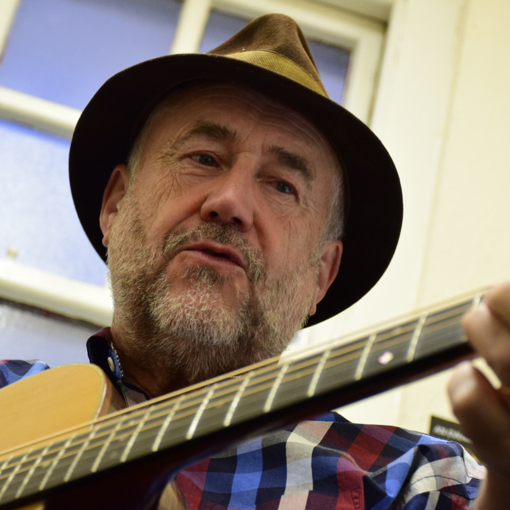 Close up of Bob Fox in a hat with a guitar