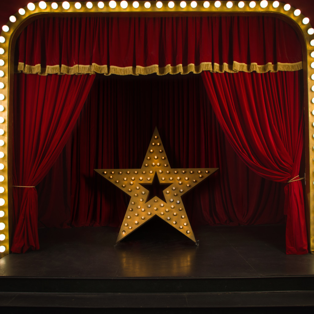 Theatre stage with red curtains and a large star sculpture covered in light bulbs