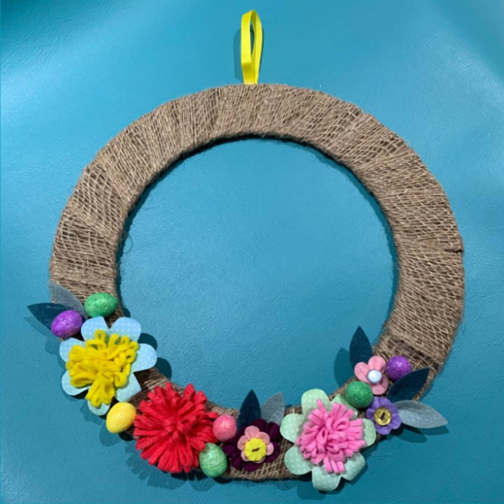 Image of a completed wreath witht he hoop wrapped in jute ribbon and decorated with colourful paper and fabric flowers and leaves