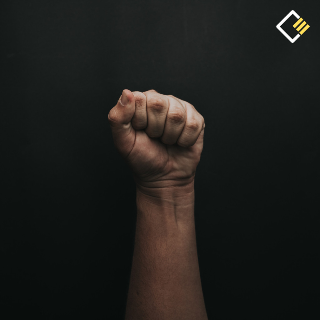 A clenched fist is raised against a dark background, symbolising strength or protest. The lighting highlights the hand's texture, conveying determination. The Cooper Education logo appears.