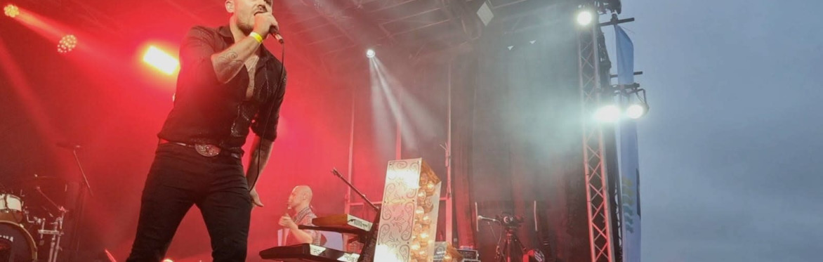 women with their hands in the air enjoying music at Buzzstock Music Festival with the Buzzstock banner showing back of stage