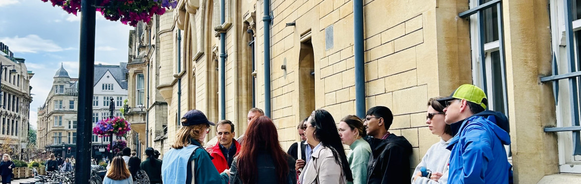 Woman standing with a tote bag next to a group of walking tour attendees next to Baliol College