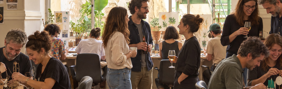 Several people involved in creative activities indoors, while some are chatting over a glass of wine during a Creative Playground Night.