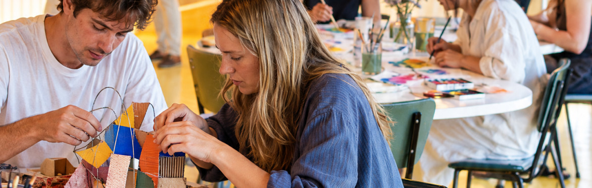 A young man and a woman are concentrated while building a sculpture of cardboard and wire together at a Creative Playground Night