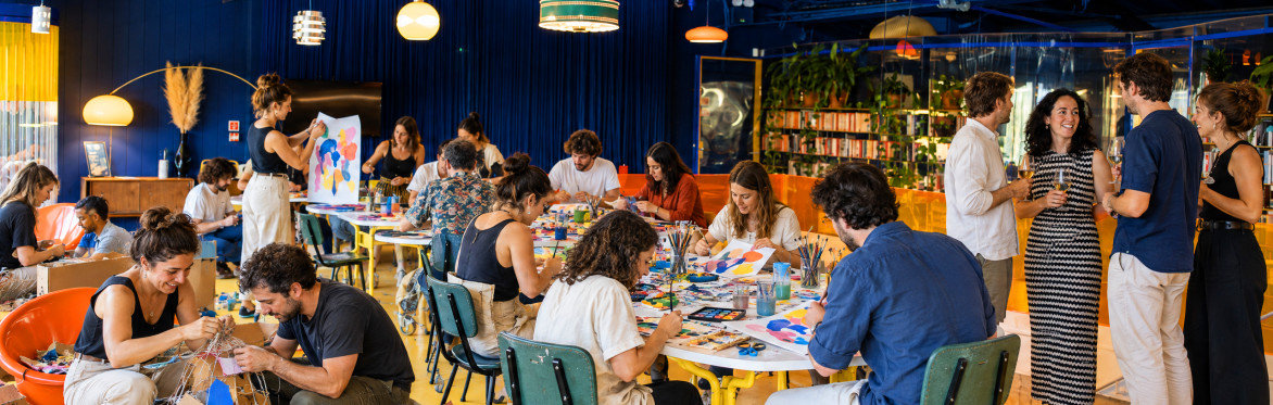A group of about 30 people creatively building sculpture from scrap materials and painting while others are having a glass of wine, at a Creative Playground Night