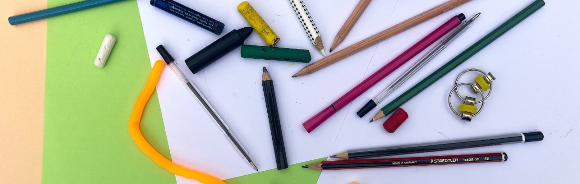 Different drawing pencils and pens. Green and cream paper in the background and fidget toys.