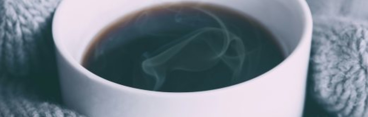 Hands wearing mittens holding a cup of steaming coffee