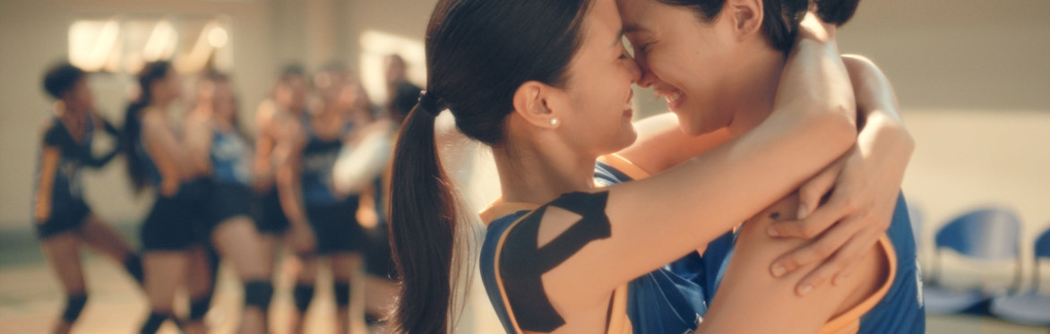 Two asian girls embrace each other in front of their volleyball team.