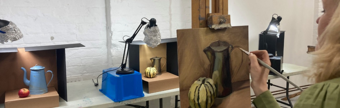Female painter standing at easel paints still life of jug and a squash