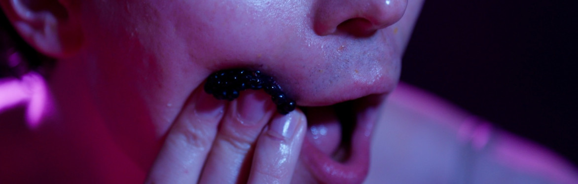 A berry is pressed into the cheek of an open-mouthed white person.