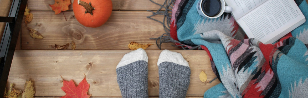 Autumn scene with leaves, blanket, coffee and feet wearing cozy socks.