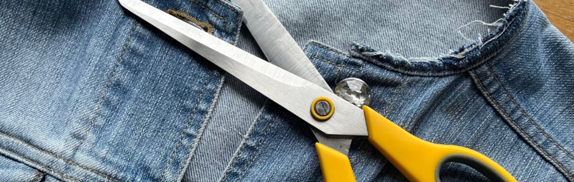 Blue denim jacket, collar had been cut off, there is a pair of yellow scissors sitting across jacket for effect only