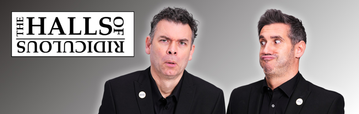 Two men in black suits pose beside an upside-down Halls of Ridiculous logo.