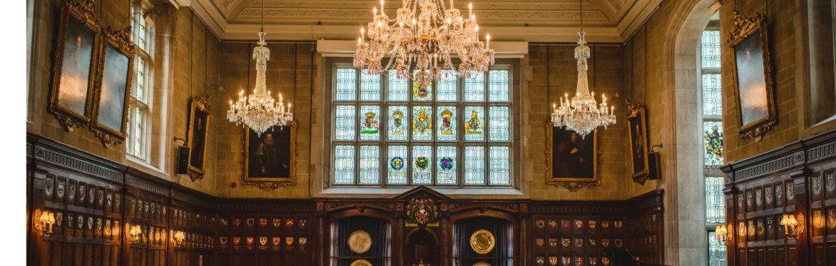 A Tudor style banqueting Hall. Wood panelled walls, colourful heraldic stained glass, ornate chandeliers and historic portraits.
