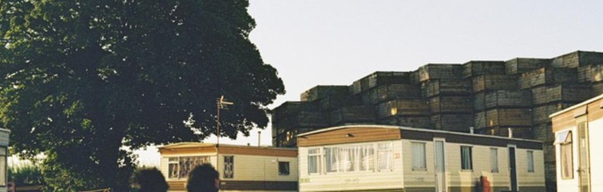 a caravan park on a sunny day next to a black geometric building that is much larger
