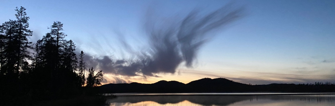 This is an image of dusk over a lake with a cloud formation that looks like a dragon of smoke