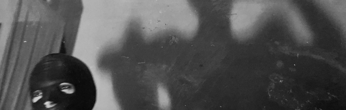 Photo of a masked person with a strong shadow behind. In black and white.