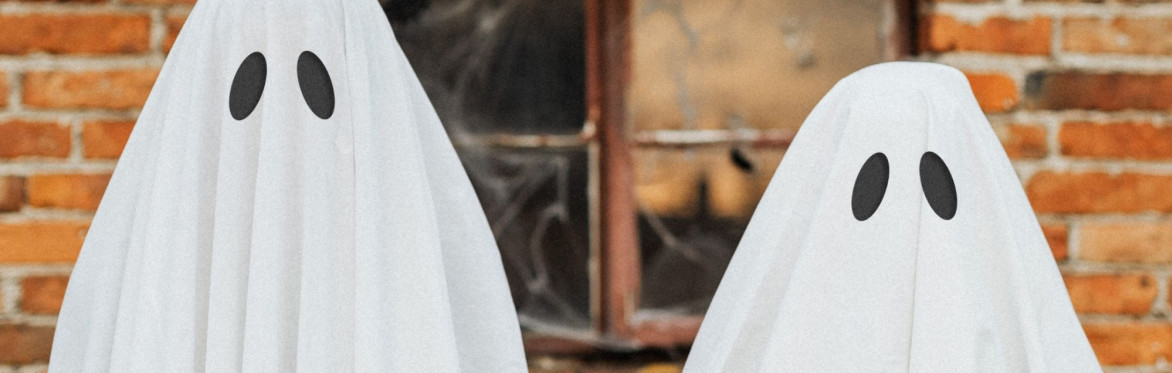 Two spooky ghosts standing in front of an abandoned building - the ghosts are people covered in white sheets with black cardboard ovals for eyes