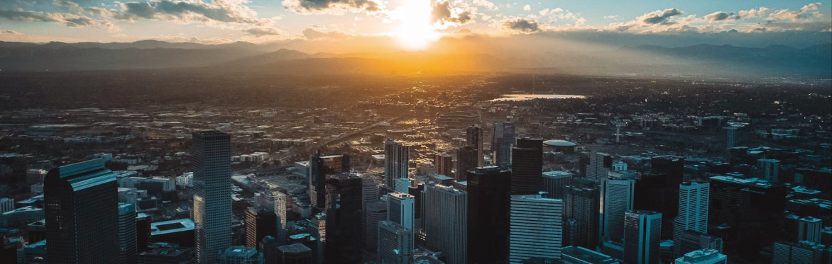 Denver skyline at sunset beneath the Rocky Mountains.