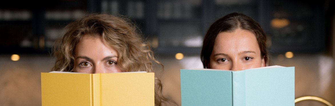 Ellie and Kathleen peer over the top of books