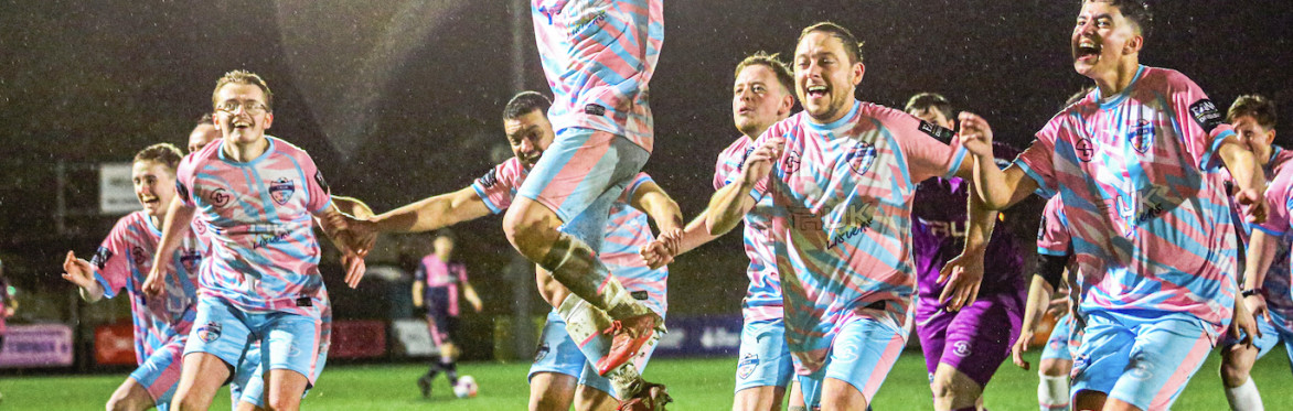 Footballers wearing trans coloured sports clothes embrace each other in celebration.