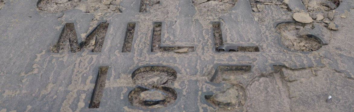 A stone brown and grey sign broken in places engraved with the lettering, Oxford Mills 1851.