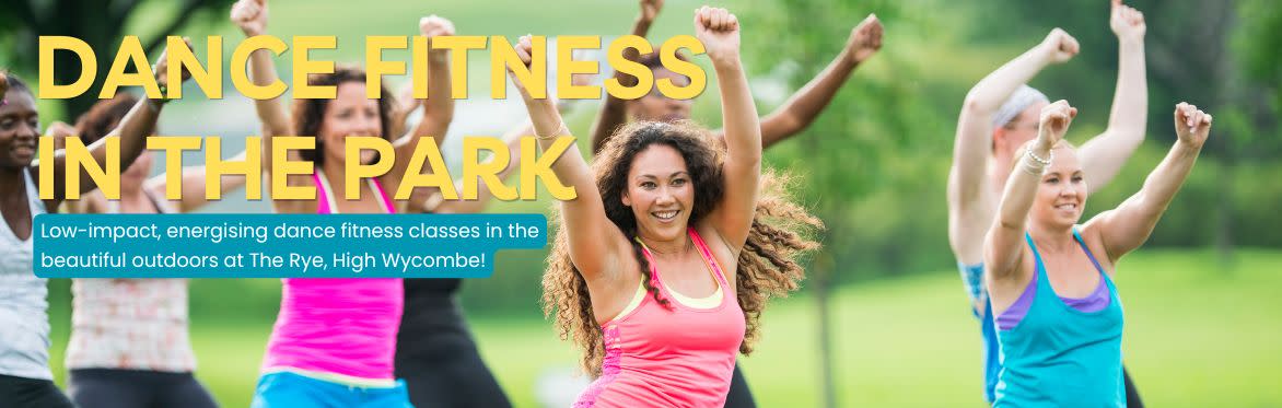 A group of women dancing with their hands in the air, dressed in fitness gear, outside in a park