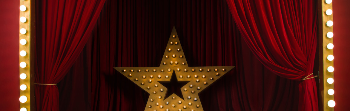 Theatre stage with red curtains and a large star sculpture covered in light bulbs