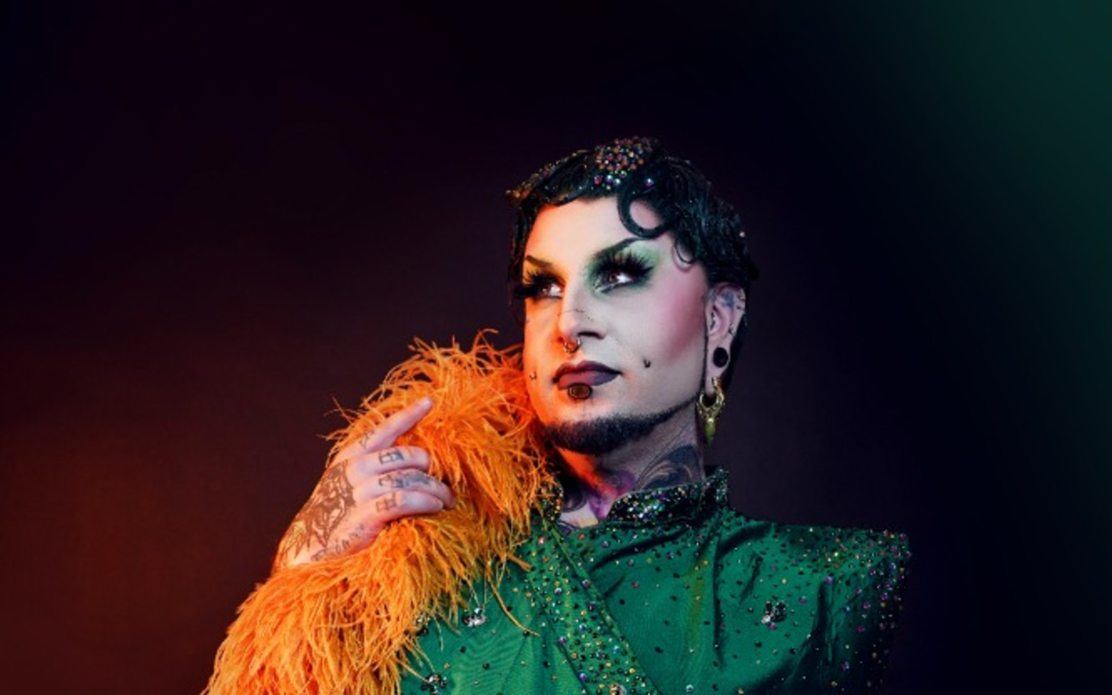 Photo is of Lou Safire looking up towards a light. They are wearing an orange boa.