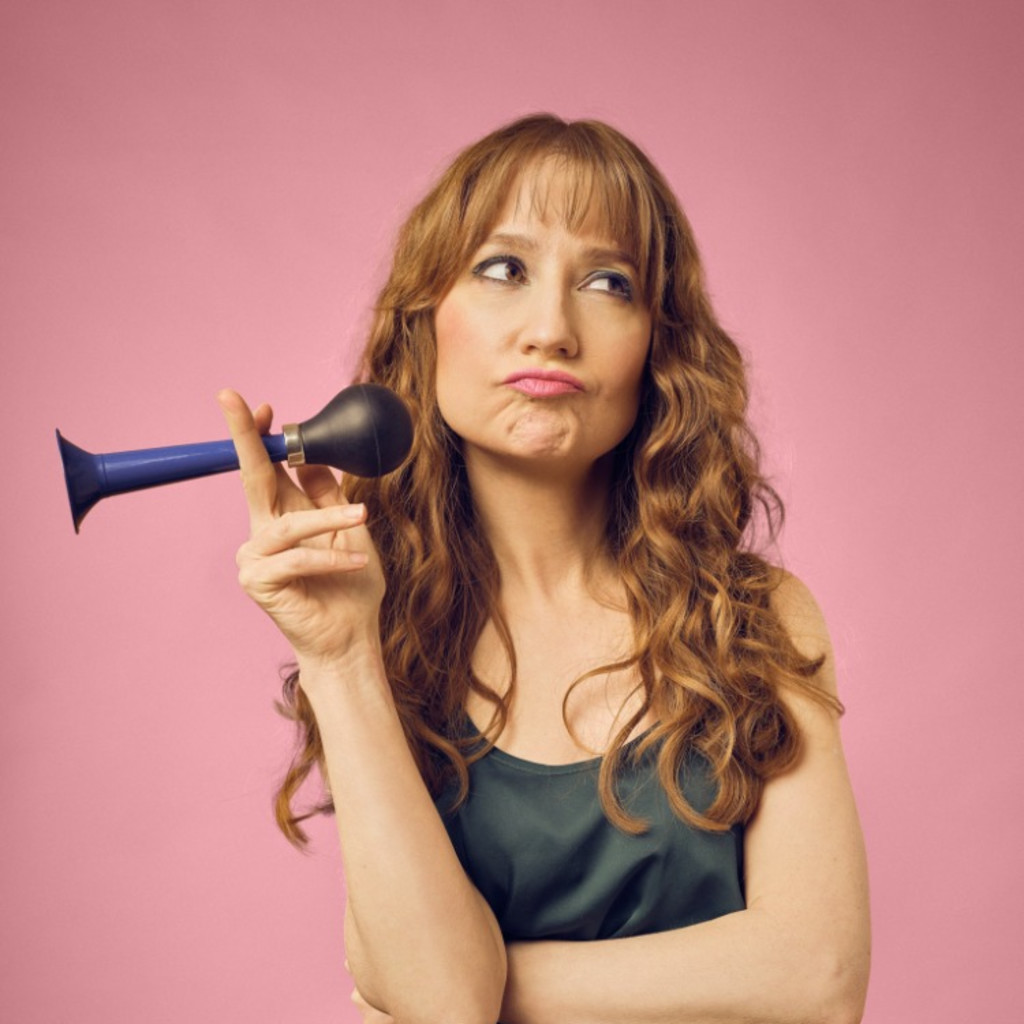 Woman with long ginger hair holds a hooter like a cigarette and pulls a face