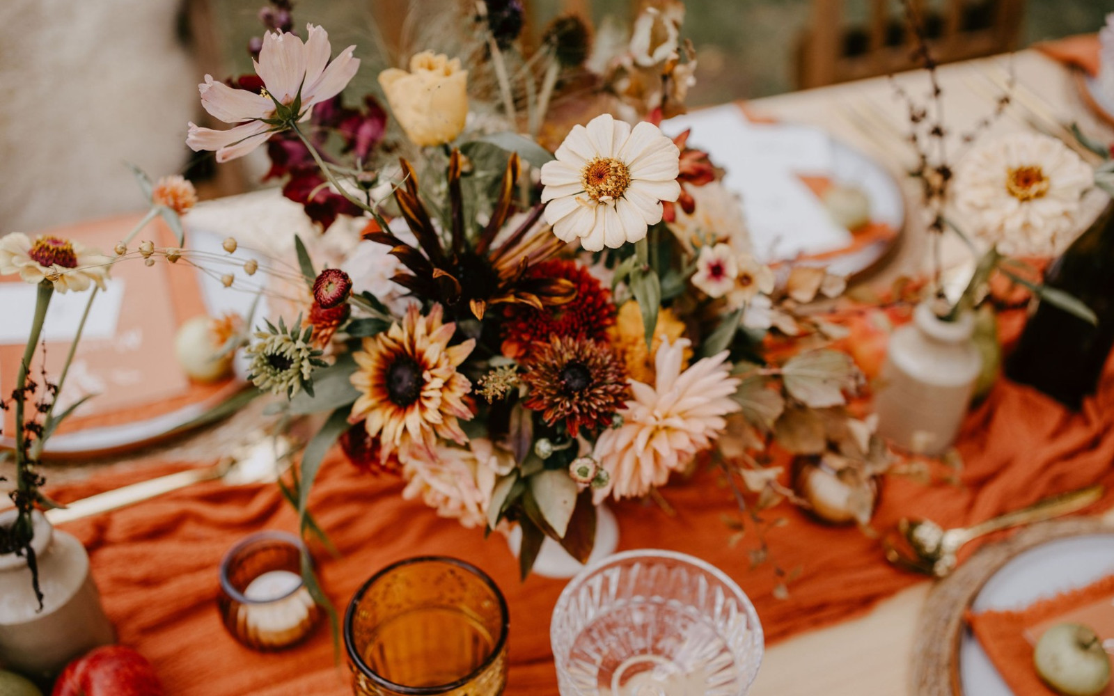 Autumnal flowers sit in the centre of a wedding table surrounded by candles and glassware