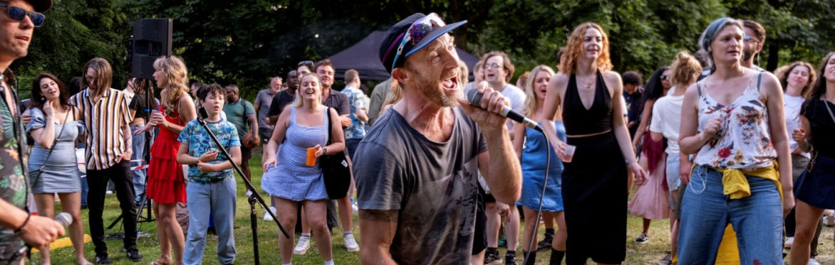A crowd watches a man singing at an outdoor karaoke event.