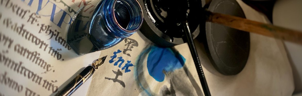 A close-up of calligraphy tools, including a blue ink bottle, an inkwell, brush and fountain pen on old handwritten papers.