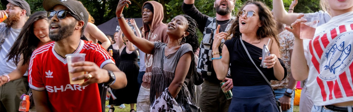 A group of men and women enjoying an outdoor music event in a park.