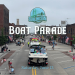 A photo of boats being pulled down a street in a boat parade.