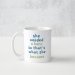 A white ceramic mug with a light blue and green text saying 'she needed a hero so that's what she became'.