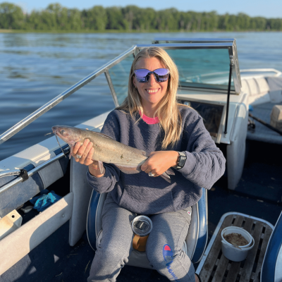 Woman wearing sunglasses and a sweatshirt in a boat holding a small catfish and smiling