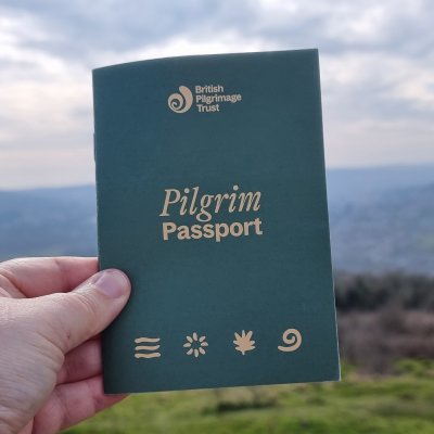 a hand holds a green pilgrim passport with a hillside in the background