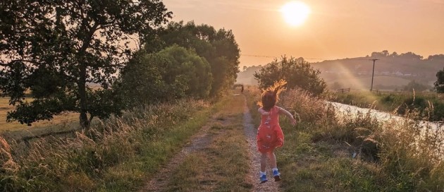 a young girl happily jumping in the air by a river with low sun