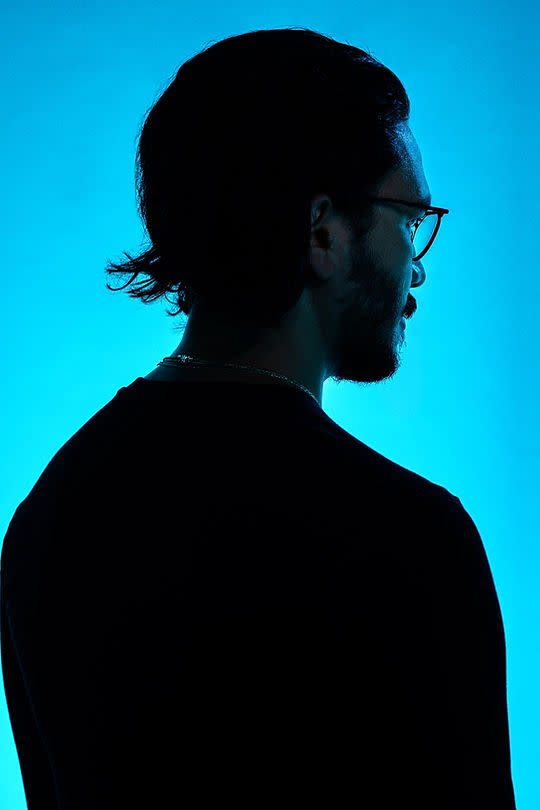 A headshot of Noel Fanaeian faced away from the camera, backlit with blue light.