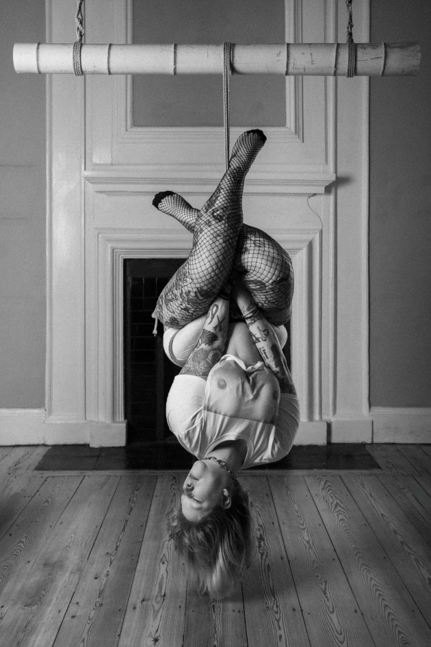 Image shows ropeyrevolver self-suspended upside down from a bamboo with her legs crossed together