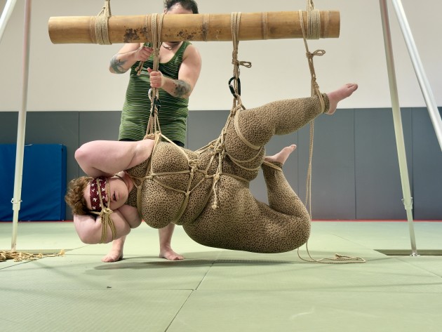 Image shows Quartz suspending Peach. Peach is suspended from bamboo on their side with a blindfold and rope covering their face.