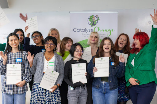 11 people smiling, holding certificates and raising hands to celebrate their graduation.