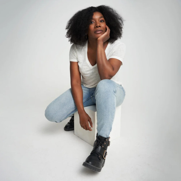 Black woman seated on a white cube posing with one hand on the chin.