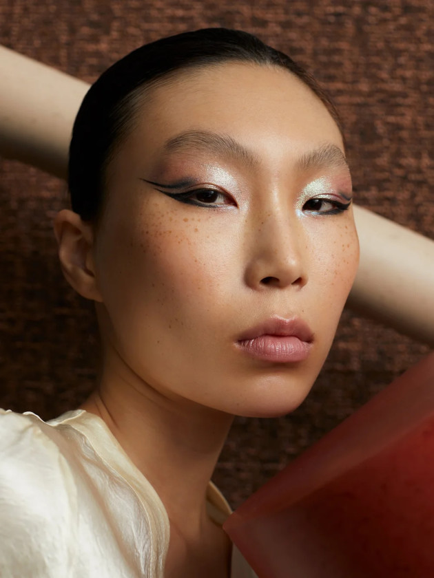 Close up headshot of model with Asian features and pink glitter/black eyeliner make up.
