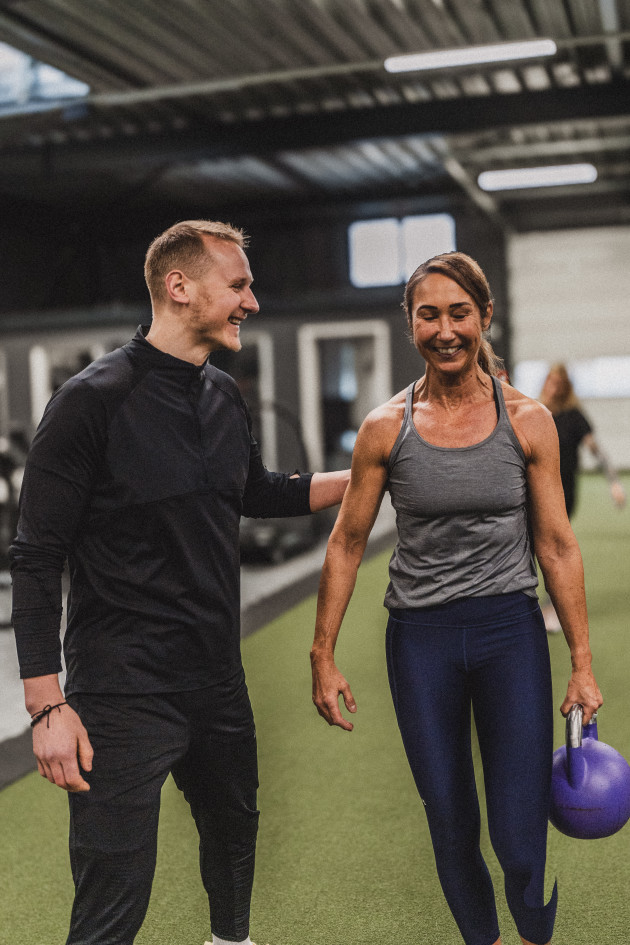 Zwei lächelnde Menschen beim gemeinsamen Training im ATMO CLUB; eine Person hält eine Kettlebell.
