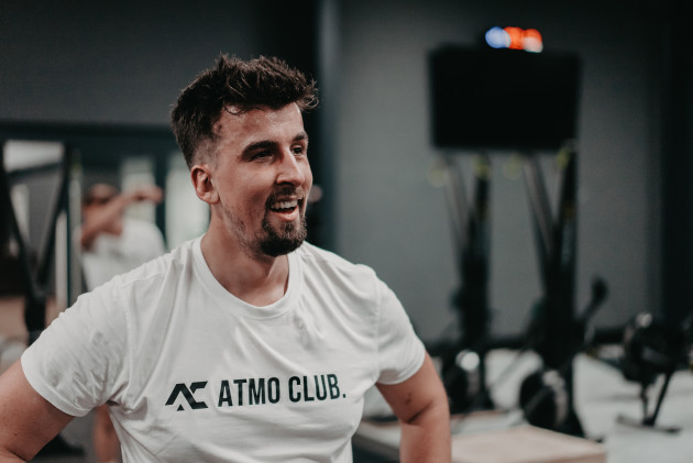 Lächelnder Trainierender im weißen ATMO-CLUB-Shirt im Trainingsbereich.